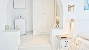 Un dormitorio minimalista con un armario blanco, una mesita de noche y un pequeño escritorio con una lámpara.