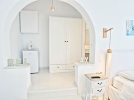 Un dormitorio minimalista con un armario blanco, una mesita de noche y un pequeño escritorio con una lámpara.