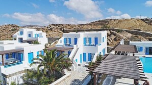 Un edificio blanco con detalles azules, una piscina y un paisaje rocoso al fondo.
