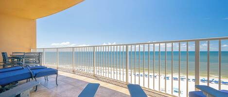A balcony with a view of the beach, equipped with lounge chairs and a table.