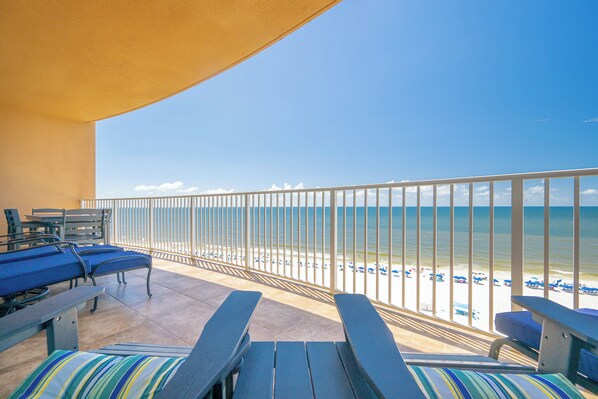 A balcony with a view of the beach, equipped with lounge chairs and a table.
