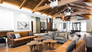 A spacious lobby with wooden flooring, leather sofas, and round coffee tables.