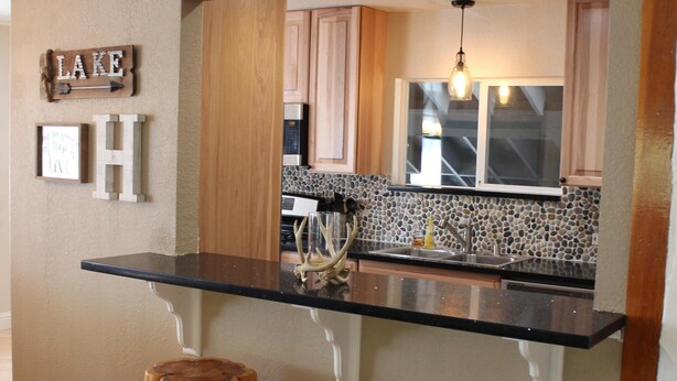 A kitchen with a black countertop, wooden stools, and a backsplash with a mosaic tile design. - Spacious Mountain Retreat, great for groups & families (Arnold)
