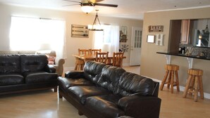 A living room with a dark brown leather sofa, a dining table with wooden chairs, and a kitchen area with wooden stools. - Spacious Mountain Retreat, great for groups & families (Arnold)