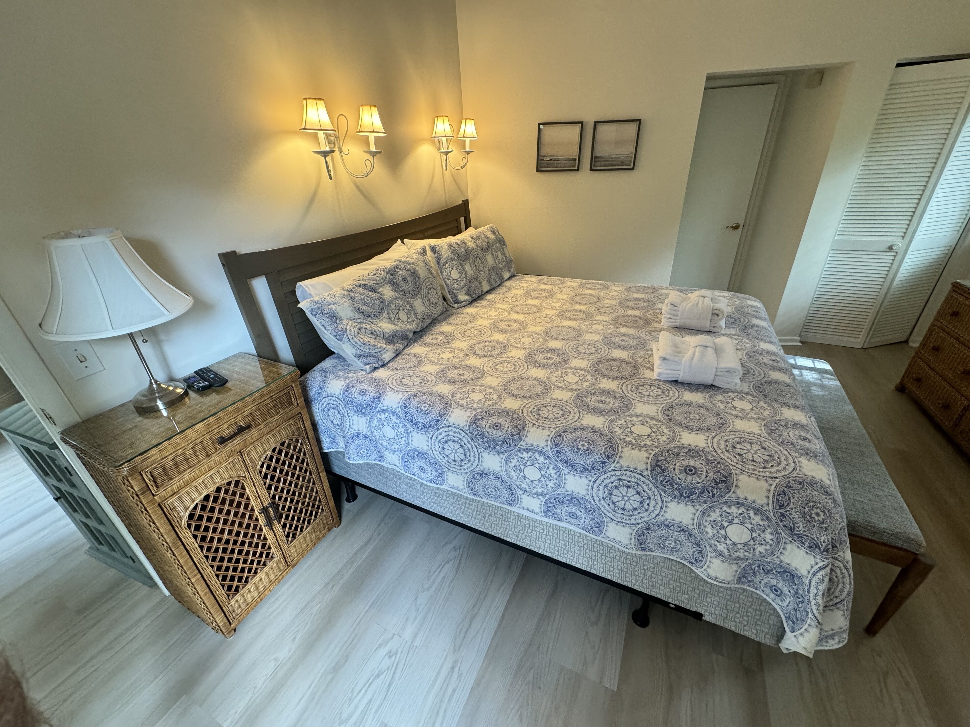 A bedroom with a bed, bedside lamp, wall-mounted lights, and a wicker nightstand.