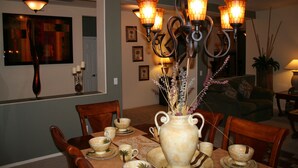 Un coin repas avec une table dressée pour quatre personnes, un vase orné de branches décoratives et un lustre à plusieurs lampes.