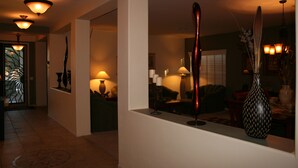 Un couloir au design intérieur moderne, agrémenté d’un grand vase posé sur un piédestal, d’un miroir qui reflète la pièce et d’une porte donnant sur un autre espace.