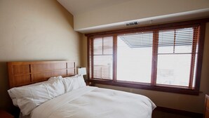 Een hotelkamer met een groot bed, een houten hoofdbord en een raam met jaloezieën.