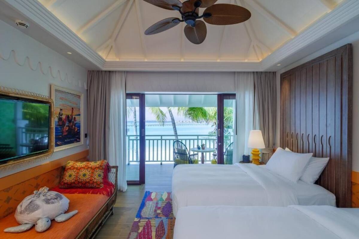 Une chambre d’hôtel avec un lit, un canapé, une télévision et un balcon donnant sur la mer.