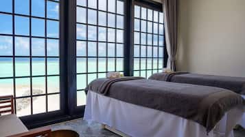 Enjoy a serene beach view from the large window, featuring two beds and a comfortable seating area.
