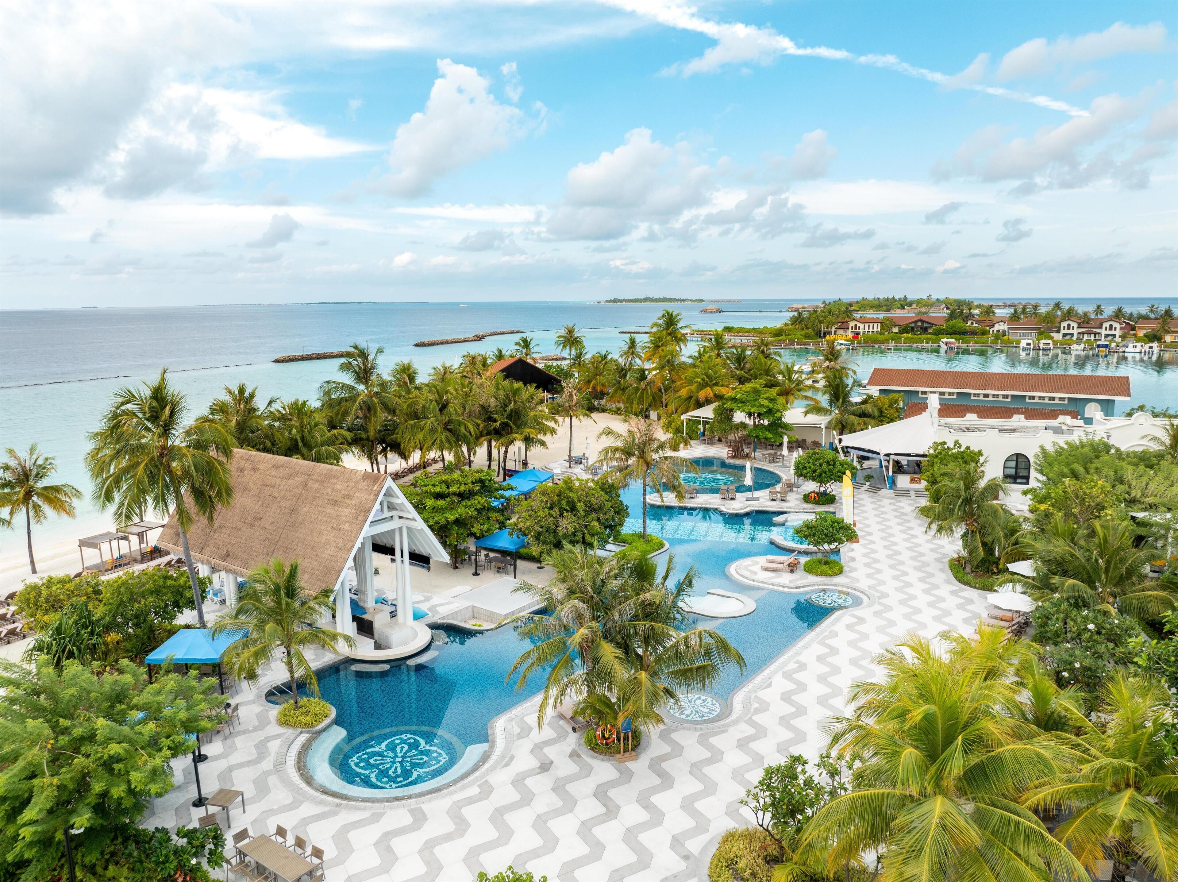 Un resort con una piscina grande, palmeras y vista al océano.