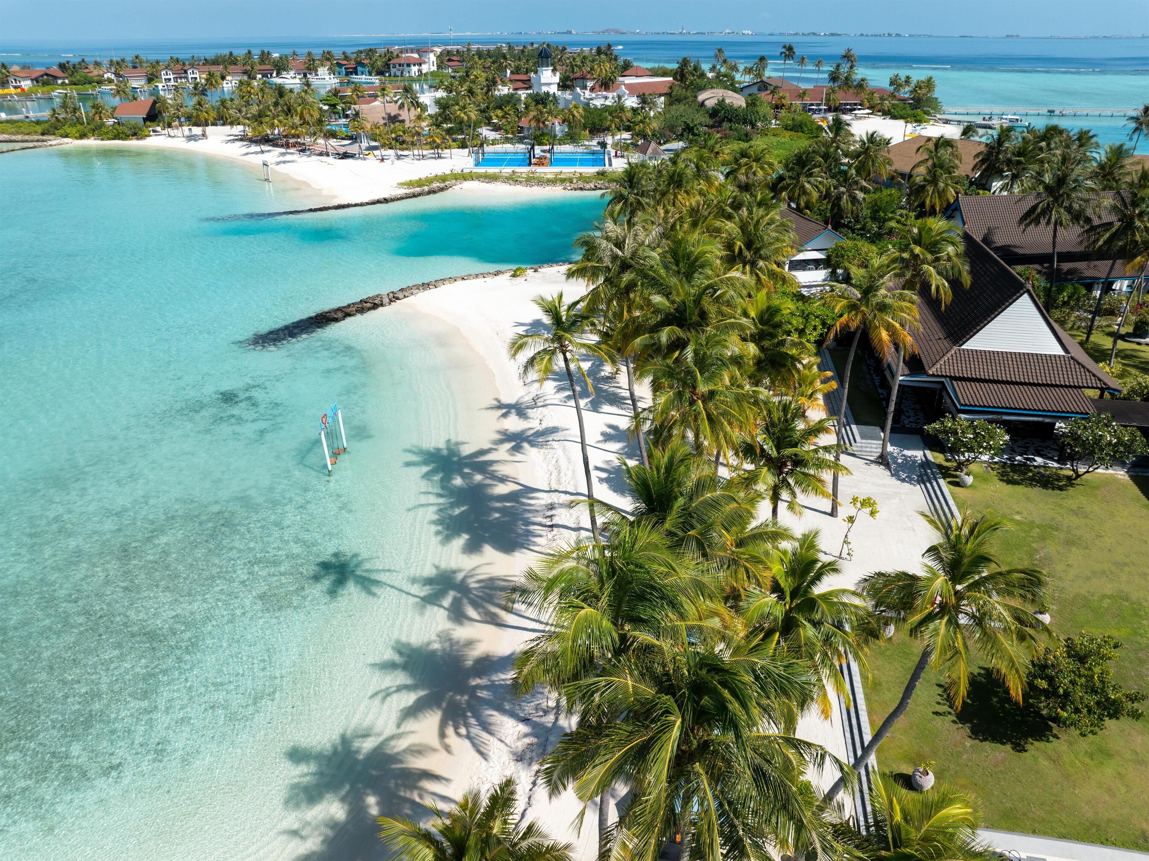 Vista aérea de un resort con playa, aguas turquesas cristalinas y palmeras.