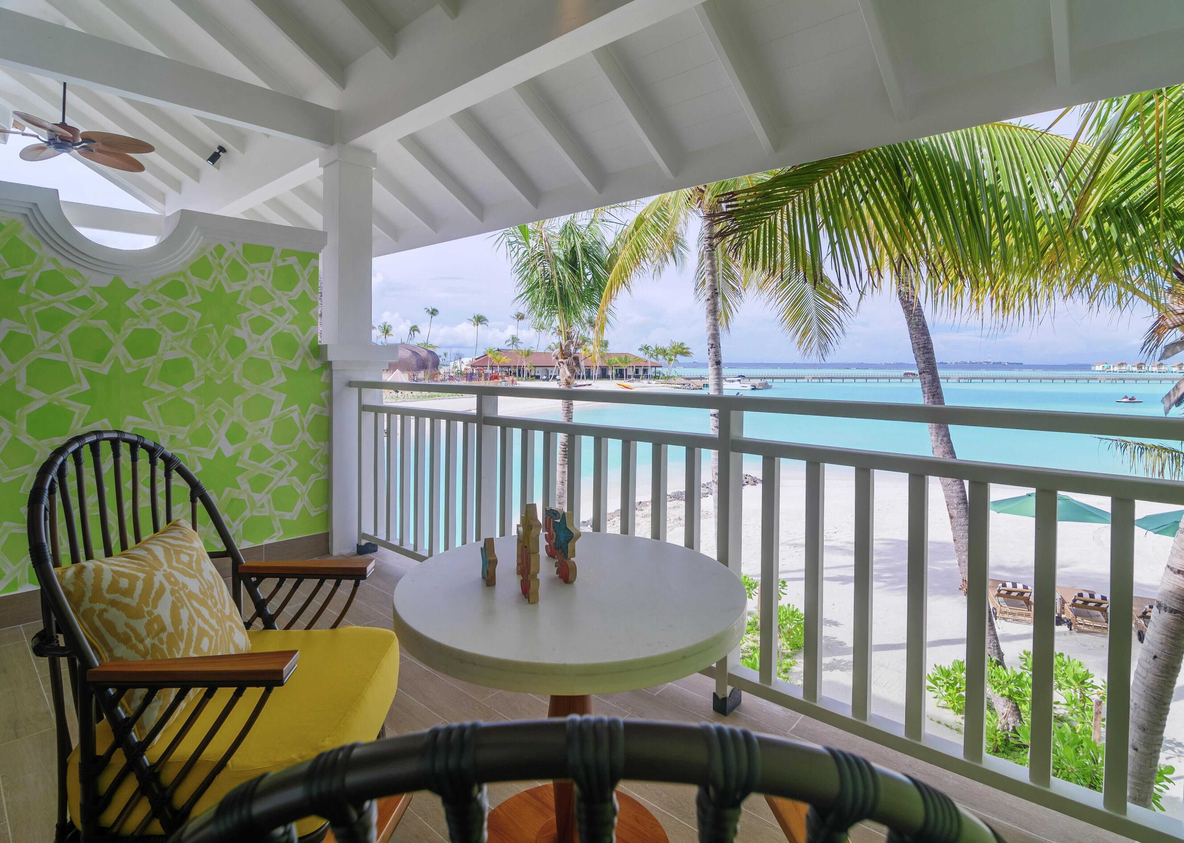 A balcony with a view of the beach, a round table, and a chair with a cushion.