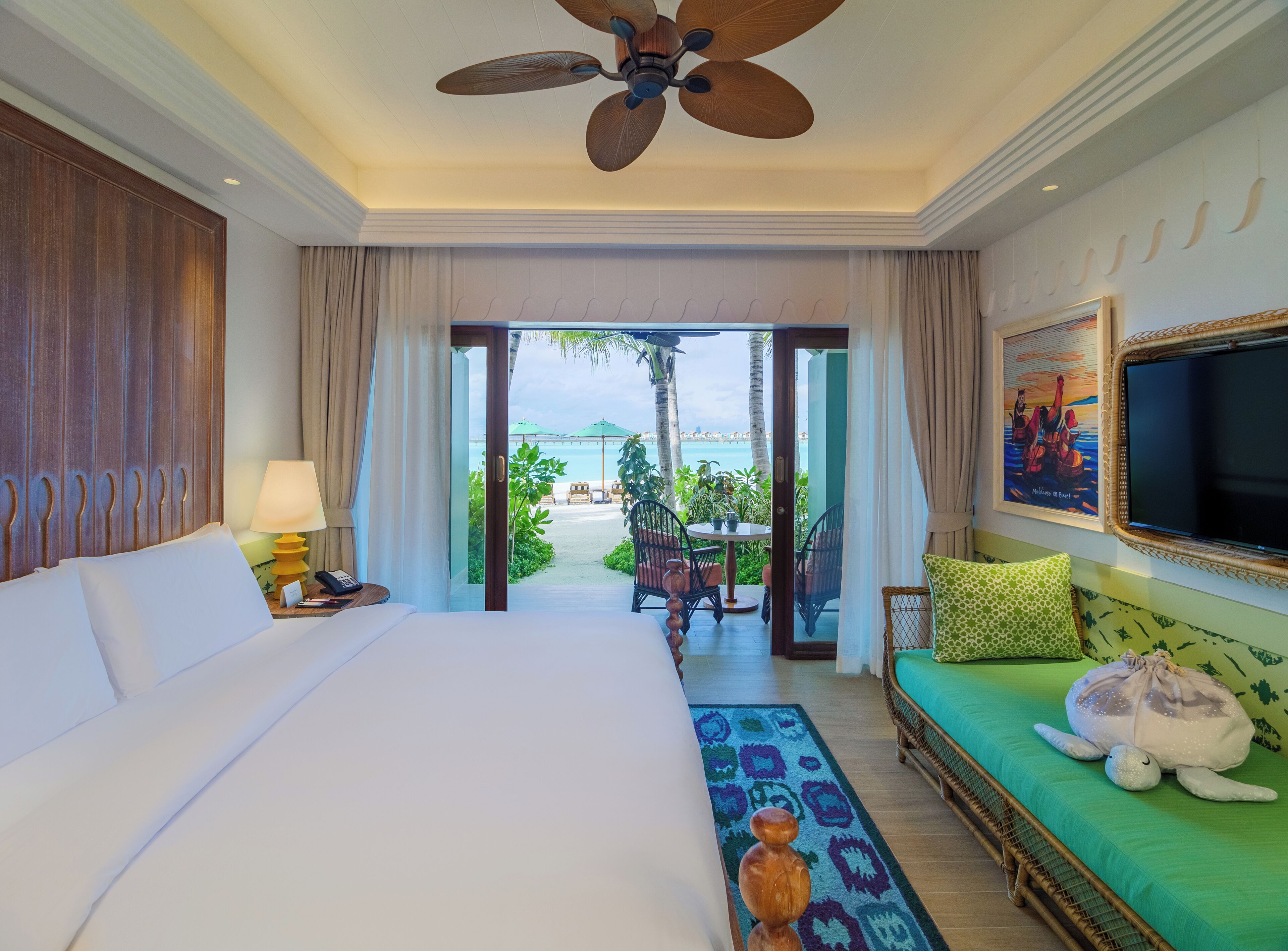 A hotel room with a bed, a green sofa, a television, and a view of the beach.
