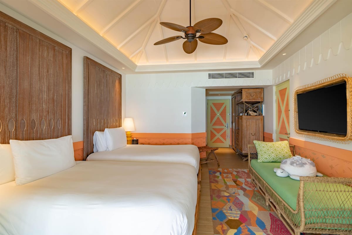 A hotel room with a large bed, a small sofa, a ceiling fan, and a television.