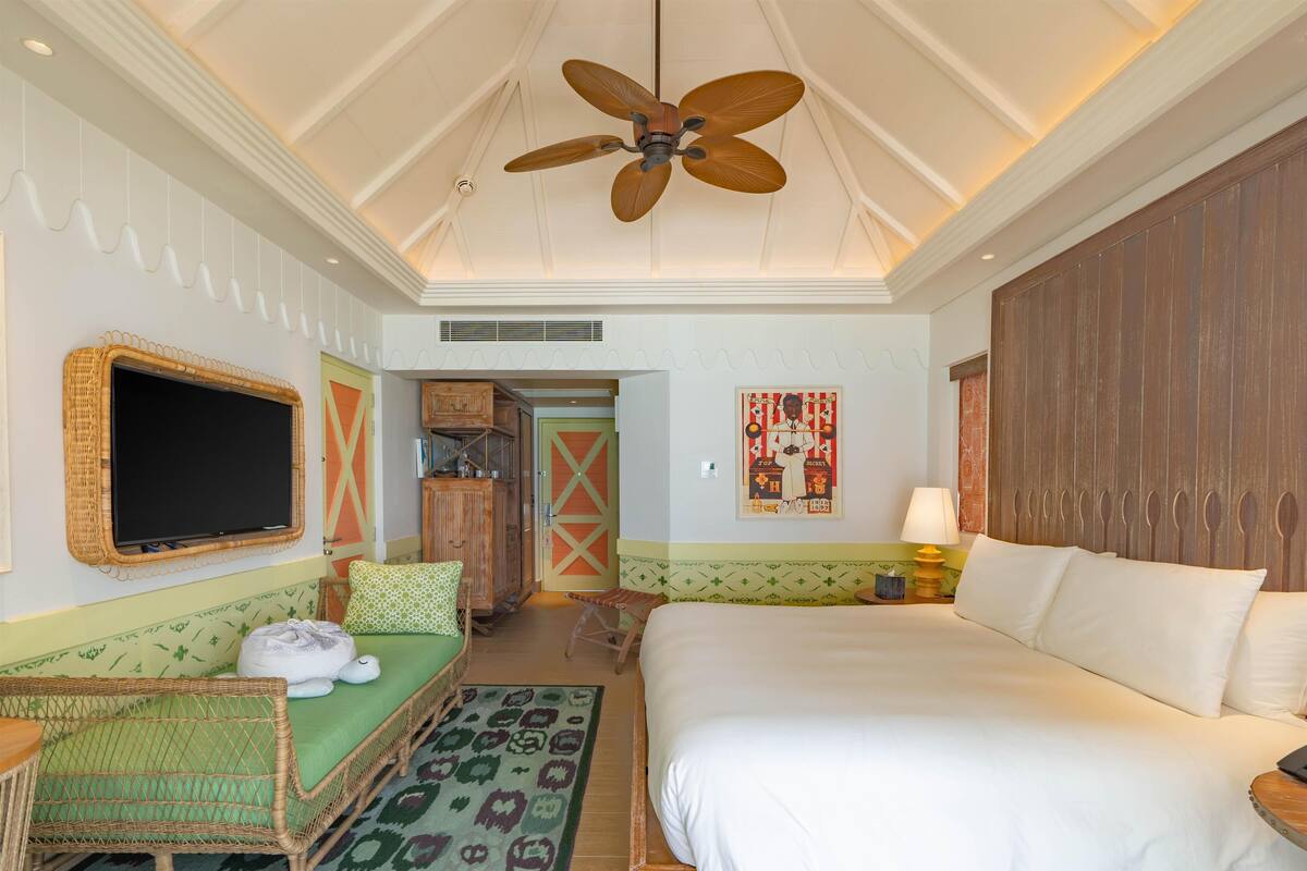 A hotel room with a large bed, a television, a ceiling fan, and a green patterned rug.