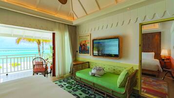 Een hotelkamer met balkon, een bed, een sofa, een televisie en uitzicht op de oceaan.