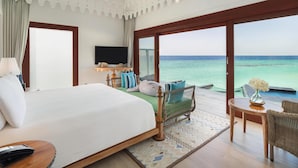 A hotel room with a large bed, a television, a view of the ocean, and a balcony with a wicker chair and table. - SAii Lagoon Maldives, Curio Collection by Hilton (Eh'mafushi)