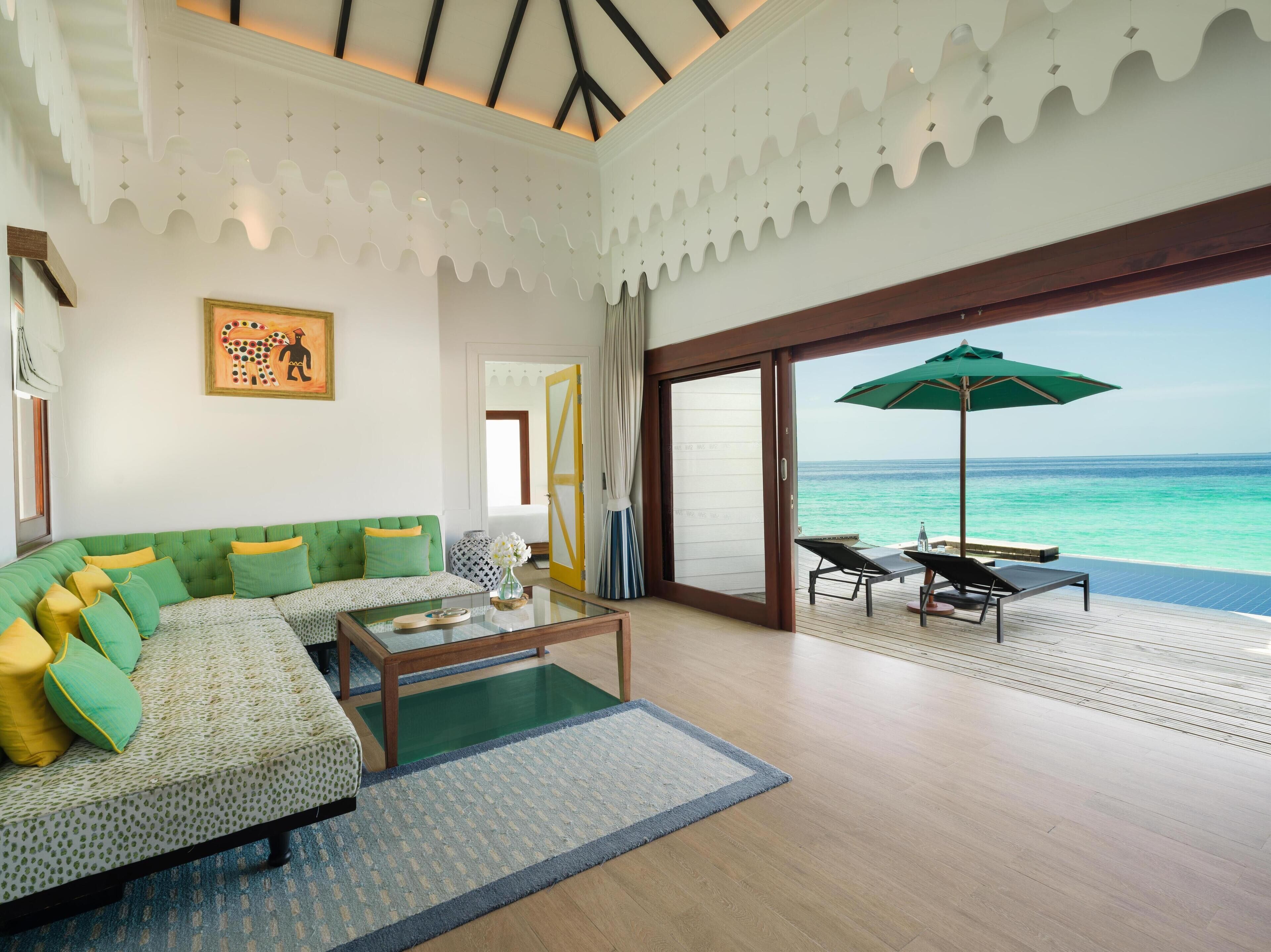 A spacious living room with a green sofa, a coffee table, and a view of the ocean through a sliding glass door.
