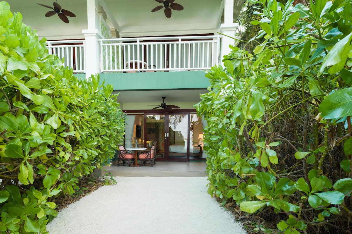A covered outdoor area with a table and chairs, surrounded by lush greenery.
