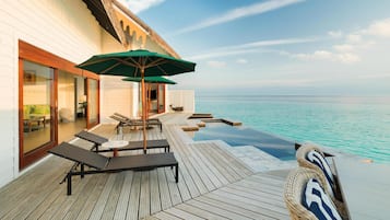 An infinity pool with a wooden deck, lounge chairs, and an umbrella.