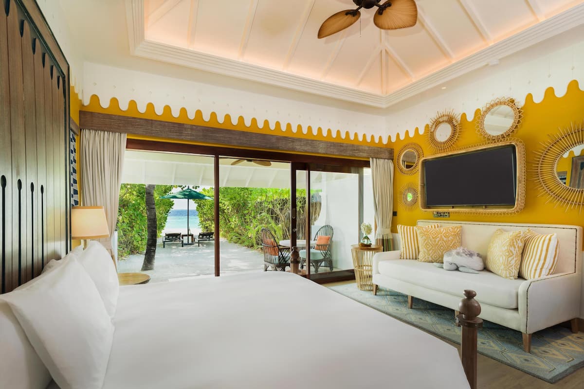 A hotel room with a large bed, a sofa, a TV, and a view of the beach.