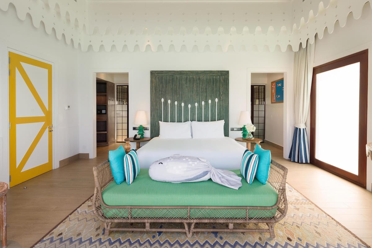 A spacious bedroom with a large bed, a green sofa, and a patterned rug.
