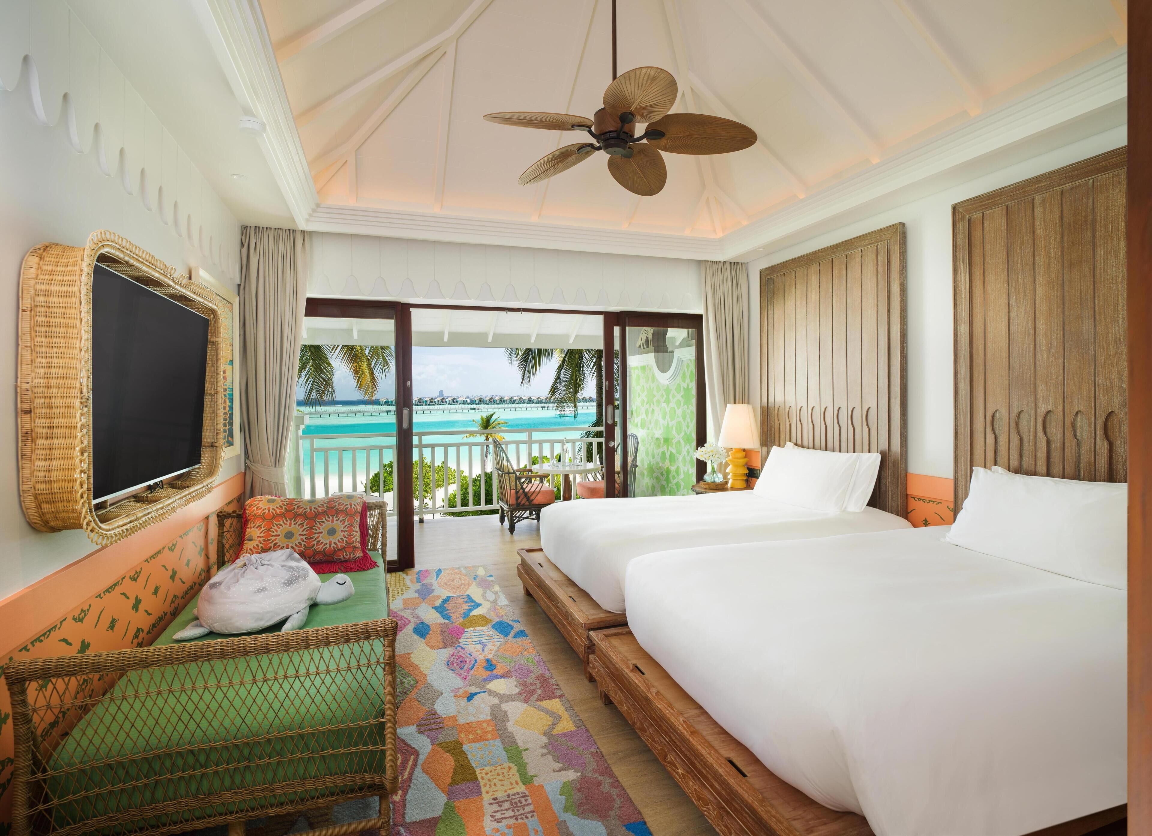 A hotel room with a bed, a chair, a TV, and a balcony with a view of the ocean.