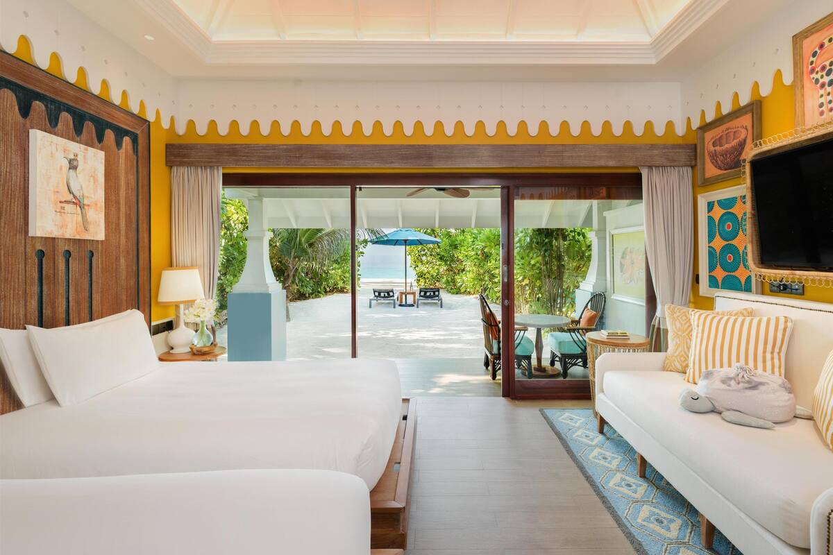 A hotel room with two beds, a sofa, a TV, and a view of a pool and garden.