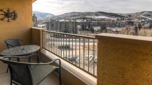 A balcony with a view of a mountainous landscape, a table with chairs, and a decorative wall piece. - Condo near Gondola! Free Shuttle (Avon)
