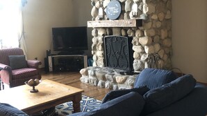 A living room with a stone fireplace, a television, a sofa, and a coffee table. - Terrific Family Getaway on Lake Charleviox with Stunning Views  (East Jordan)