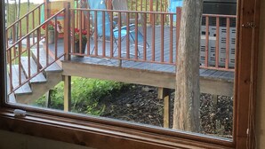 A view from a window overlooking a deck with a railing, a tree, and a blue chair. - Terrific Family Getaway on Lake Charleviox with Stunning Views  (East Jordan)
