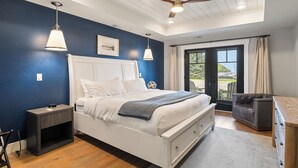 A bedroom with a white bed, a ceiling fan, a nightstand, a gray sofa, and a view of the outdoors through a sliding glass door.