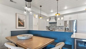 A modern kitchen with white cabinets, a blue bench, and a stainless steel refrigerator.