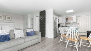 A modern living room with a grey sofa, white chairs, and a kitchen area with white cabinets and a black brick accent wall. - Beach & Tennis Getaway 3206 (Bonita Springs)
