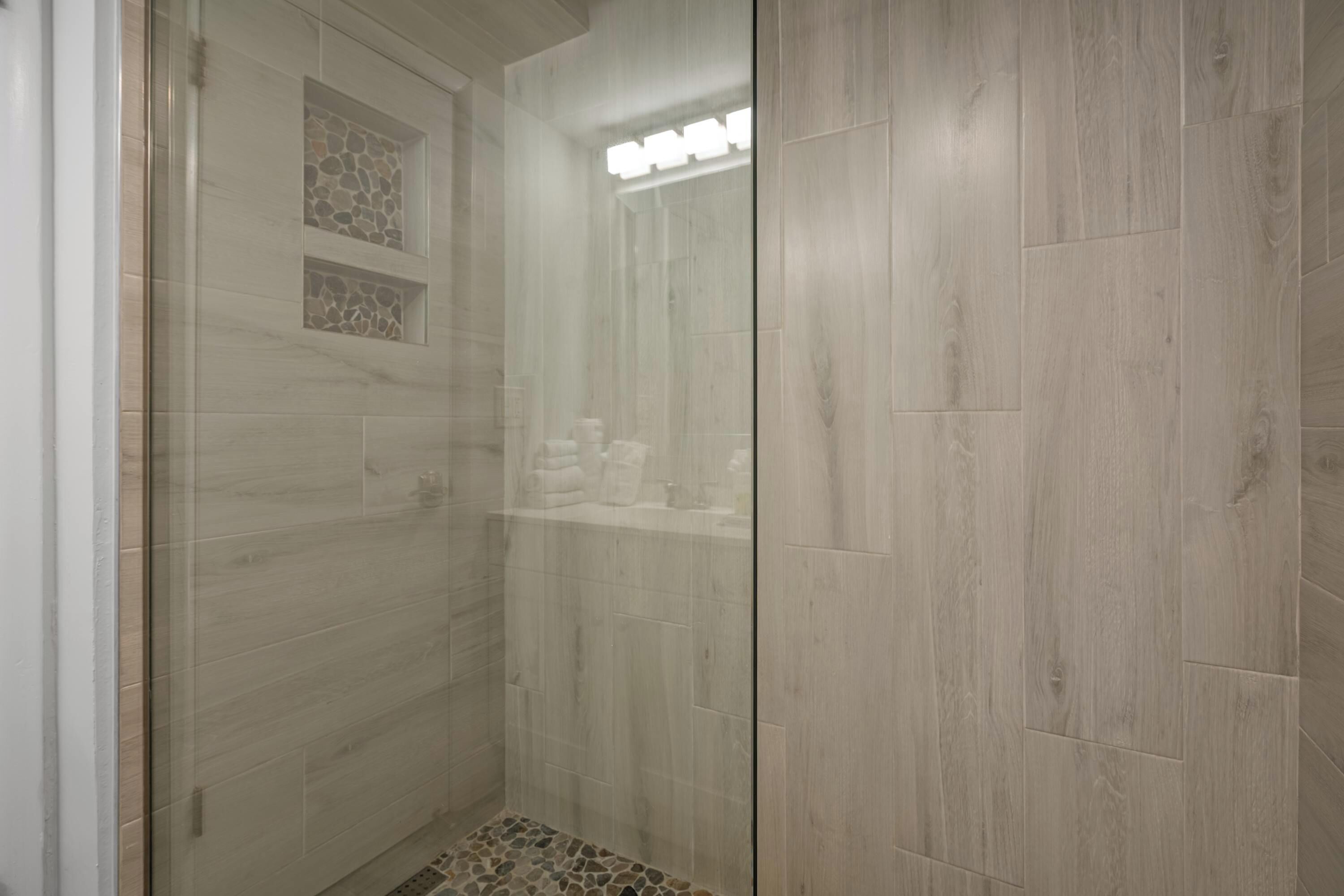 Une douche à l’italienne avec une porte en verre, des murs carrelés et un sol en bois.