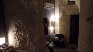 Una habitación de paredes de piedra con una cama, una silla, un escritorio y un espejo.