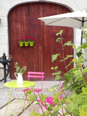 Een terras met een houten deur, een witte parasol en een tafel met een vaas vol bloemen.
