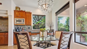 A modern kitchen with wooden cabinets, a glass dining table, and a chandelier. - Experience luxury at Paramount, featuring stunning mountain views, a large pool and game room! (Indio)