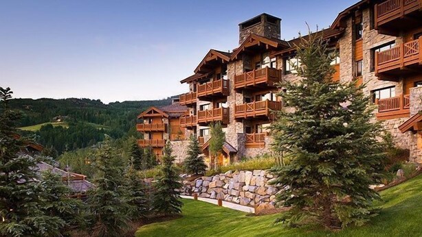 A multi-story lodge with wooden balconies and stone walls, surrounded by lush greenery and a hilly landscape. - Condo with Gas Fireplace and Spacious Rooms (Cordillera)