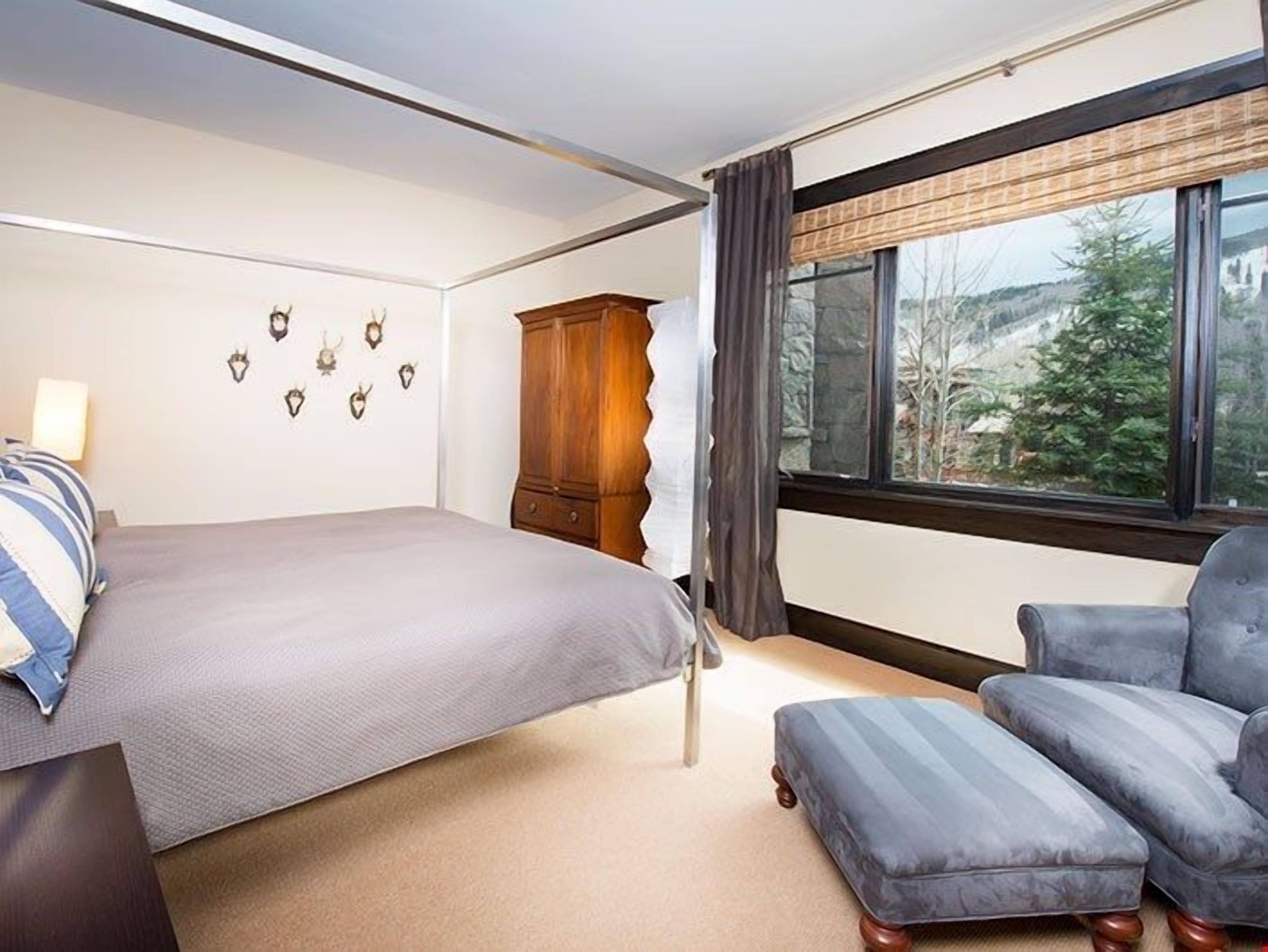 A bedroom with a bed, a wardrobe, a chair, and a window with a view of trees.