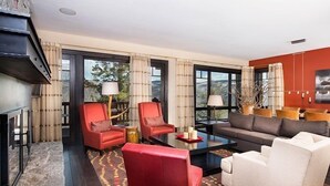 A modern living room with a fireplace, red and white chairs, a grey sofa, and large windows offering a view of the outdoors. - Condo with Gas Fireplace and Spacious Rooms (Cordillera)