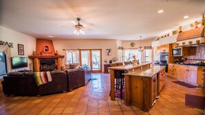 A spacious living room with a fireplace, a large sofa, and a television. There is a kitchen area with wooden cabinets and a tiled floor. - Rancho Privado Tucson AZ (Tucson)