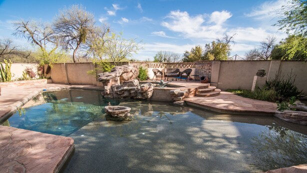 A swimming pool with a natural rock design, surrounded by a patio area with chairs and a table. - Rancho Privado Tucson AZ (Tucson)