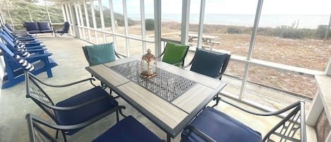Ett takförsett utomhusområde med bord och stolar, med utsikt över en strand.