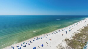 Uma praia com fileiras de guarda-sóis e espreguiçadeiras, mar azul límpido e areal dourado.