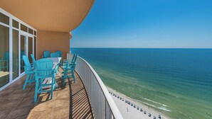 Varanda com cadeiras azul-turquesa e uma mesa com vista para uma praia com guarda-sóis.