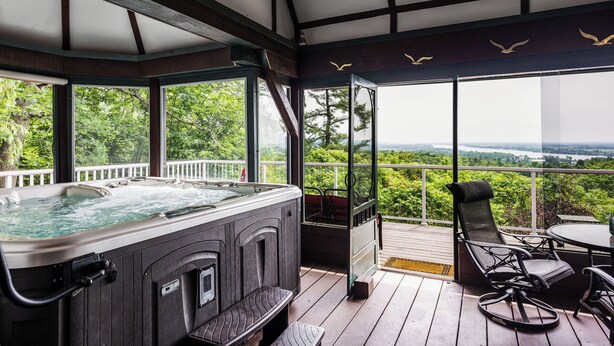 A hot tub on a wooden deck with a view of a forest and a lake.