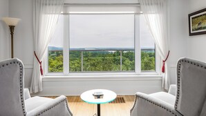 A room with a large window, two chairs, a small table, and a lamp.