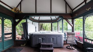 A hot tub in a covered outdoor area with a wooden deck, a chair, and a small step stool.